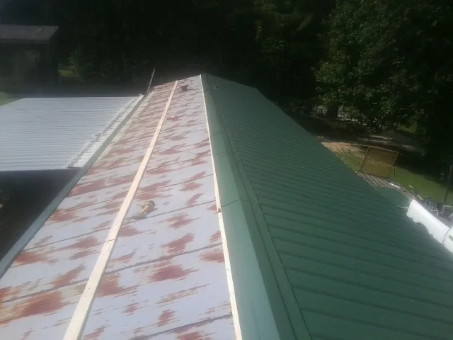Old rusted panels beside newly installed green metal roofing — Wind Damage Roof Repair by Roofing Brothers in Red Rock
